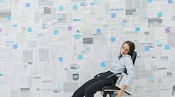 woman asleep on a chair in front of wall of business papers