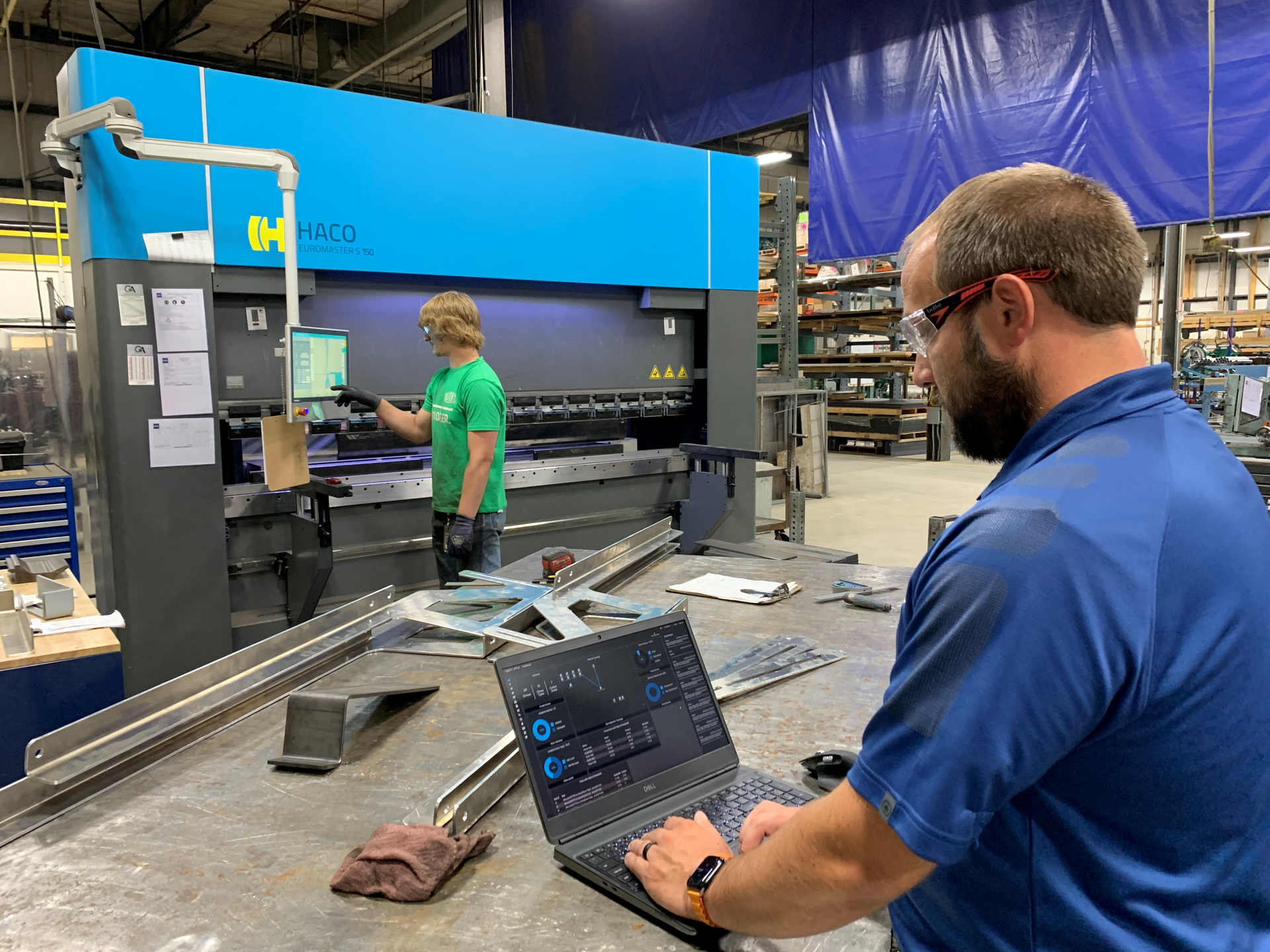 Dave Smit, senior systems analyst at Interstates (right), examines the network traffic dashboard and communication settings in Veracity OT Network Controller software at the system integrator&rsquo;s prefabrication shop in Sioux Center, Iowa, while Jace Mulder, production technician (left), operates the Haco press break. OT Network Controller manages a software-defined network (SDN) switch from Dynics, and uses zero-trust and deny-by-default methods, which enables Interstates to improve network visibility and security for the machine and enhance operational efficiency. Source: Interstates