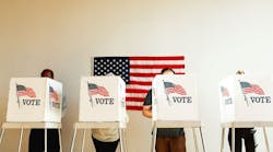 U.S. election day; people at voting booth at U.S. election station with American flag in background. U.S. election day; people at voting booth at U.S. election station with American flag in background.