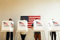 U.S. election day; people at voting booth at U.S. election station with American flag in background. U.S. election day; people at voting booth at U.S. election station with American flag in background.