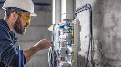 A male electrician works in a switchboard with an electrical connecting cable. A male electrician works in a switchboard with an electrical connecting cable.