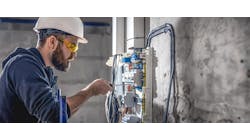 A male electrician works in a switchboard with an electrical connecting cable. A male electrician works in a switchboard with an electrical connecting cable.