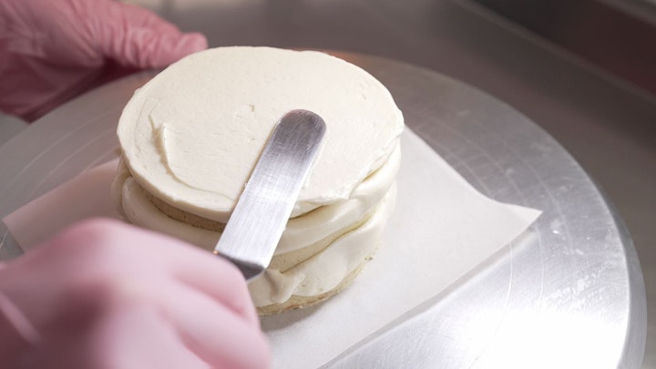 Female professional hands levels cream on baked sponge cake using metallic pastry scraper