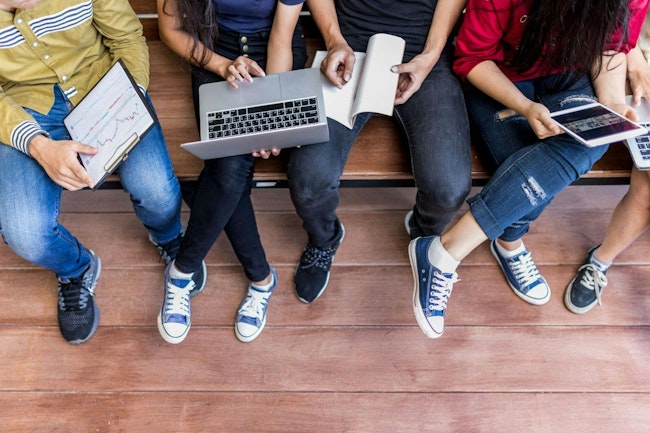 Young men and women sitting relaxed use tablet ,computer notebook on a wooden bench in college.Students using technology to learn the lessons of the student group during semester