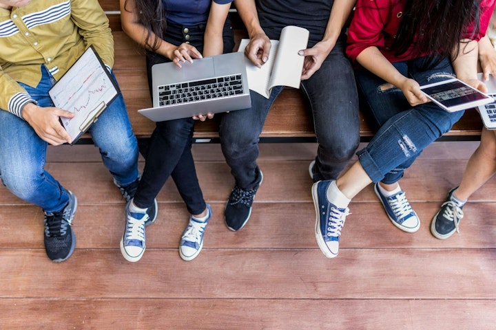 Young men and women sitting relaxed use tablet ,computer notebook on a wooden bench in college.Students using technology to learn the lessons of the student group during semester