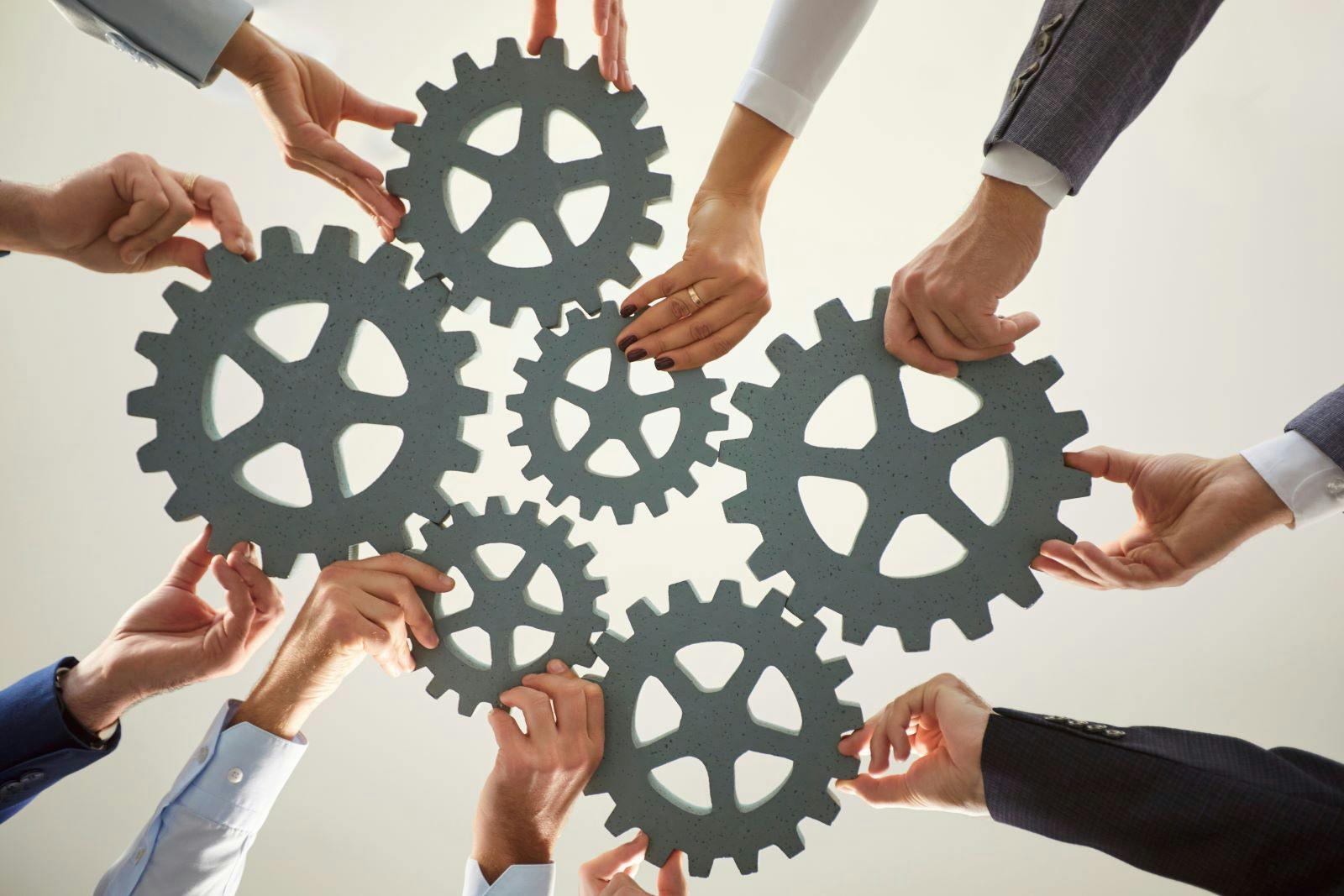 Hands from diverse individuals work together to arrange large gears on a surface, symbolizing cooperation and collective effort for success in a business environment.