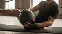 Side view of crop unrecognizable athletic male doing side twist exercise with medicine ball during intense functional training in gym Side view of crop unrecognizable athletic male doing side twist exercise with medicine ball during intense functional training in gym