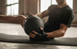 Side view of crop unrecognizable athletic male doing side twist exercise with medicine ball during intense functional training in gym Side view of crop unrecognizable athletic male doing side twist exercise with medicine ball during intense functional training in gym