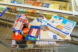 A shopping cart full of food items including pizza, cheese, and meat. The cart is in a store and the items are in the freezer section. A shopping cart full of food items including pizza, cheese, and meat. The cart is in a store and the items are in the freezer section.