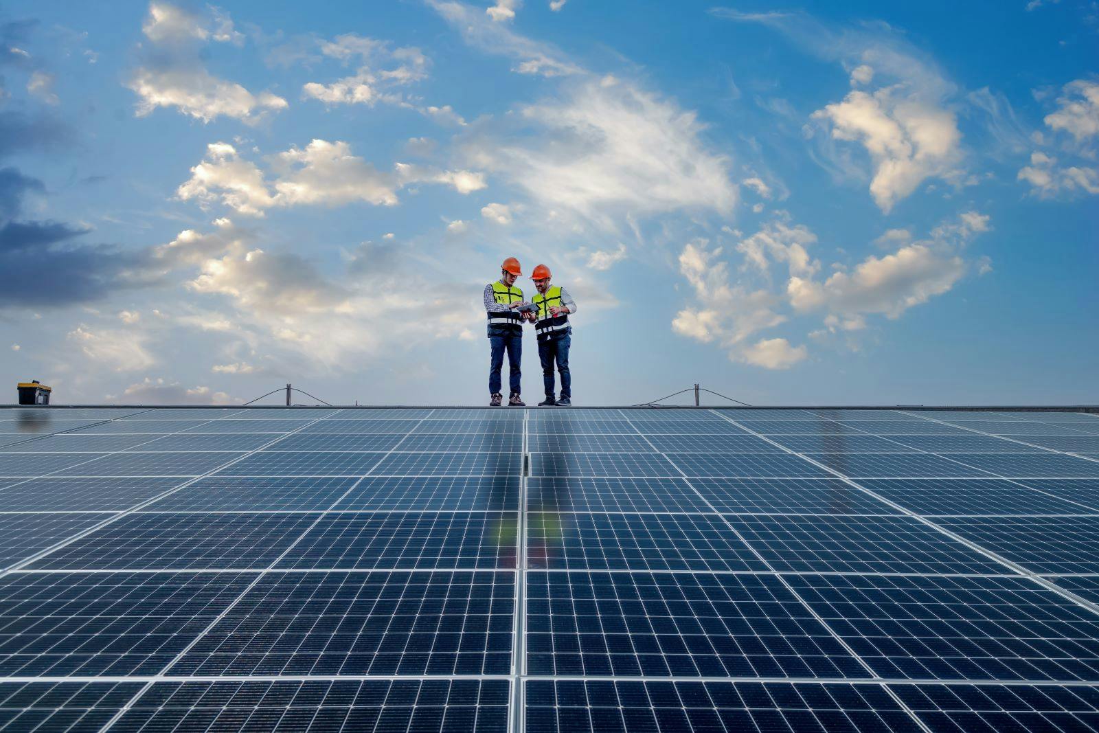 Engineers walking on roof inspect and check solar cell panel by holding equipment box and radio communication