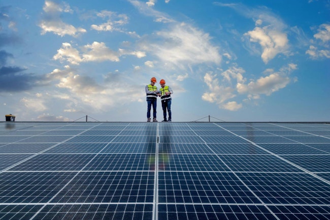 Engineers walking on roof inspect and check solar cell panel by holding equipment box and radio communication