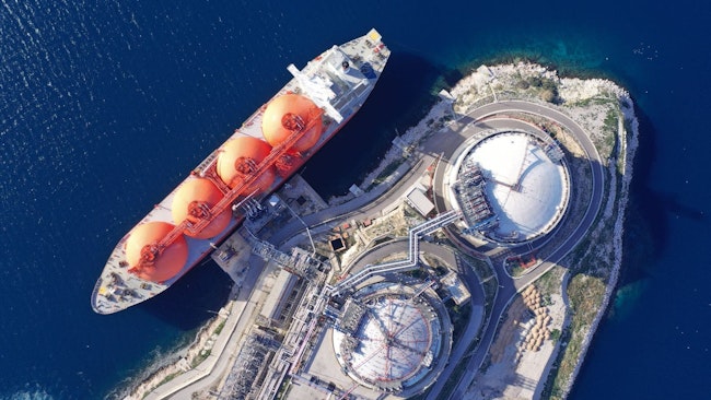 Aerial drone top down photo of LNG (Liquified Natural Gas) tanker anchored in small gas terminal island with tanks for storage to store and regasify LNG