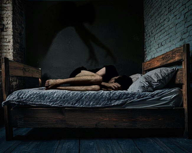 This image captures the chilling essence of sleep paralysis: a person curled in fear, with a shadowy hand looming overhead, symbolizing the helplessness and terror of the experience.