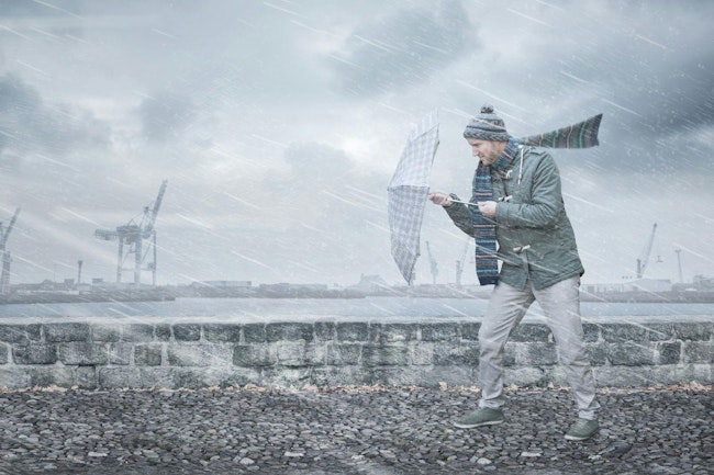 Pedestrian with an umbrella is facing strong wind and rain on a dockside