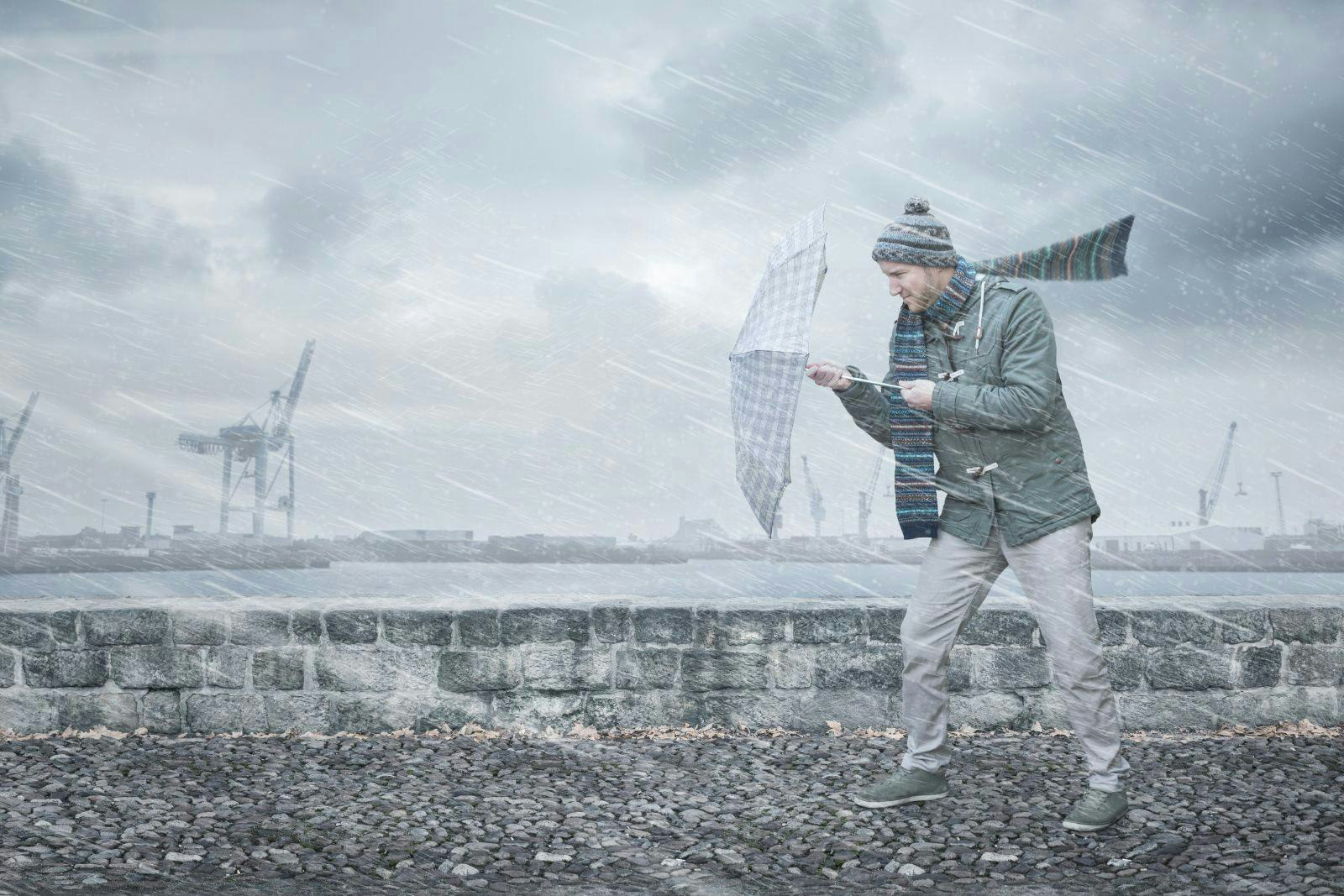 Pedestrian with an umbrella is facing strong wind and rain on a dockside
