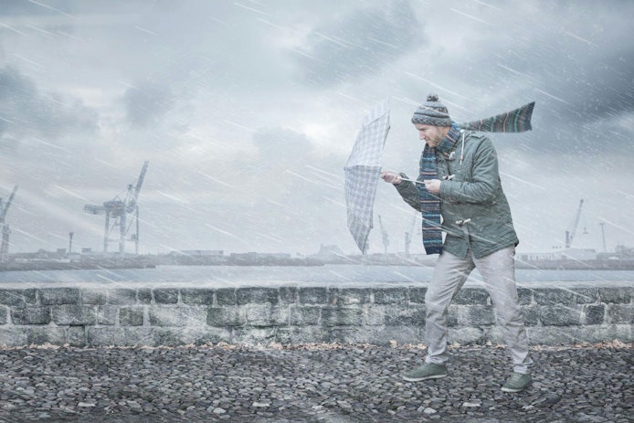 Pedestrian with an umbrella is facing strong wind and rain on a dockside