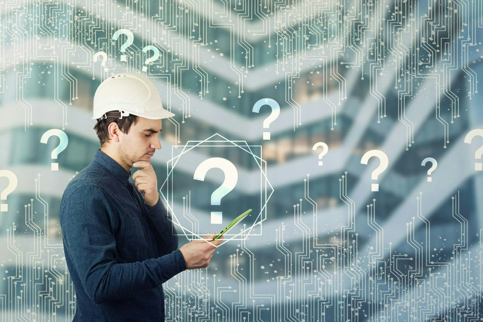 Puzzled engineer wearing protective helmet using a tablet computer gadget looking thoughtful to get answer to many questions. Science searching and interrogation virtual marks. Modern technology.