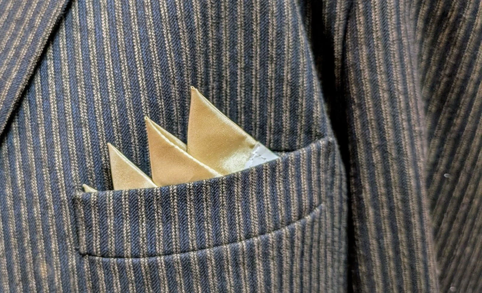 satin pocket square is tucked into a pin stripe suit coat pocket. photo is closeup.
