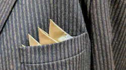 satin pocket square is tucked into a pin stripe suit coat pocket. photo is closeup.