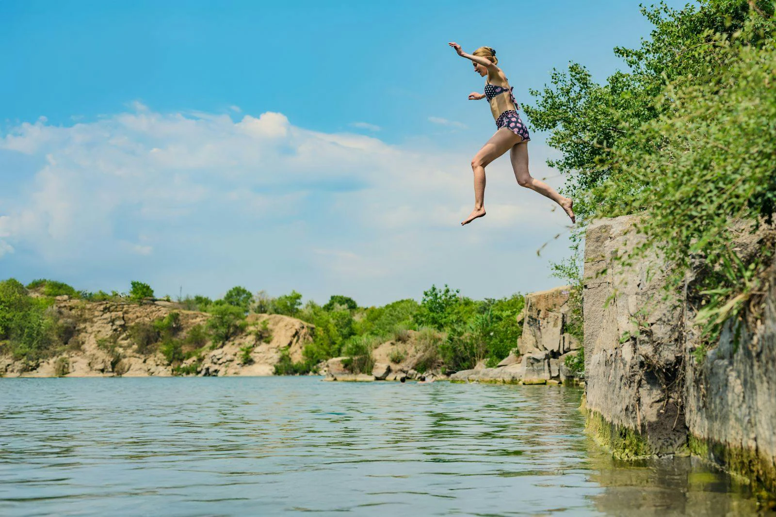 Woman in swimsuit jumps off cliff into lake
