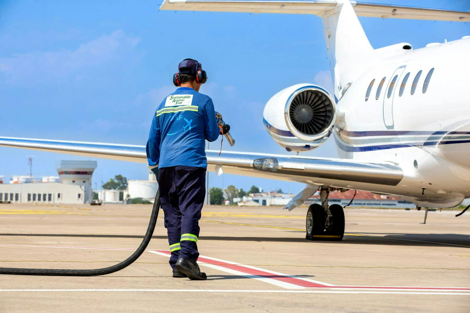 Technician refueling private jet with sustainable aviation fuel at the airport.
