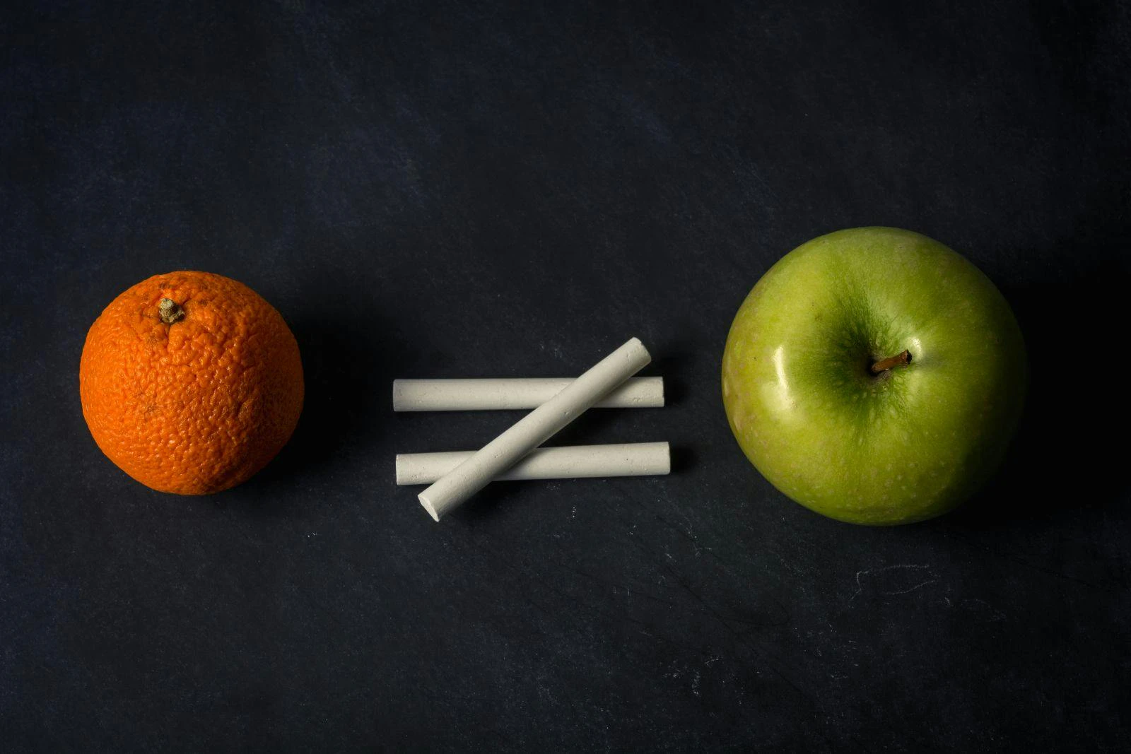 Orange does not equal apple with chalk on top of chalkboard suggesting inequality in different fruit