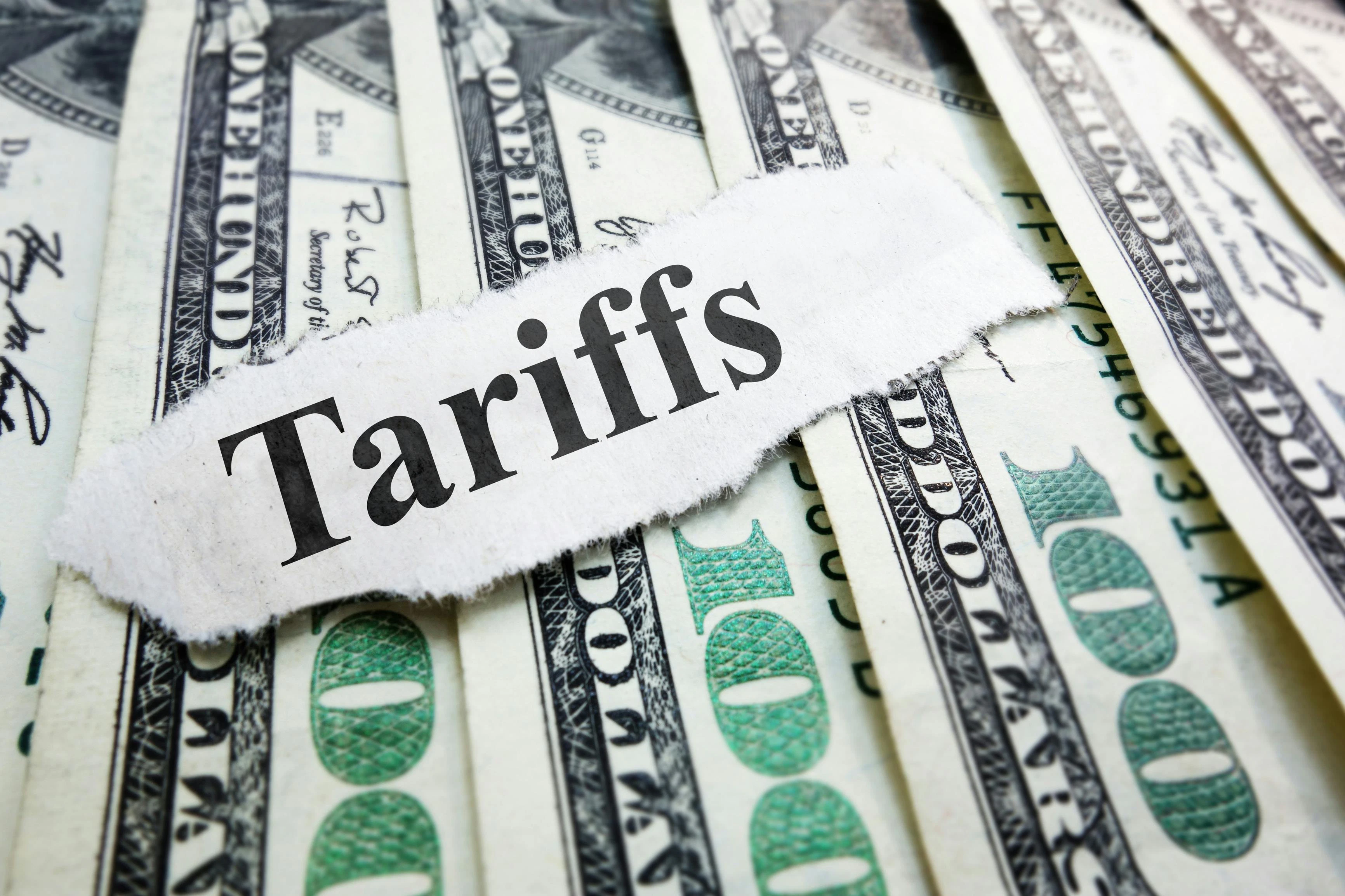 The word Tariffs typed on a scrap of paper laid atop several $100 bills