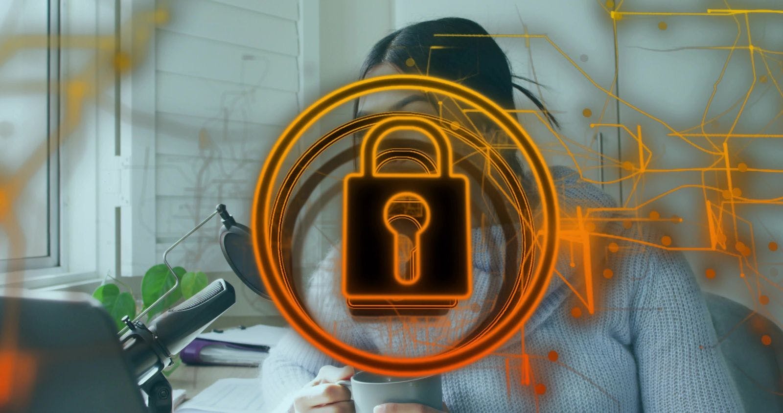 Holding mug, woman wearing gray chunky sweater sitting at home desk, with mic and padlock overlay.