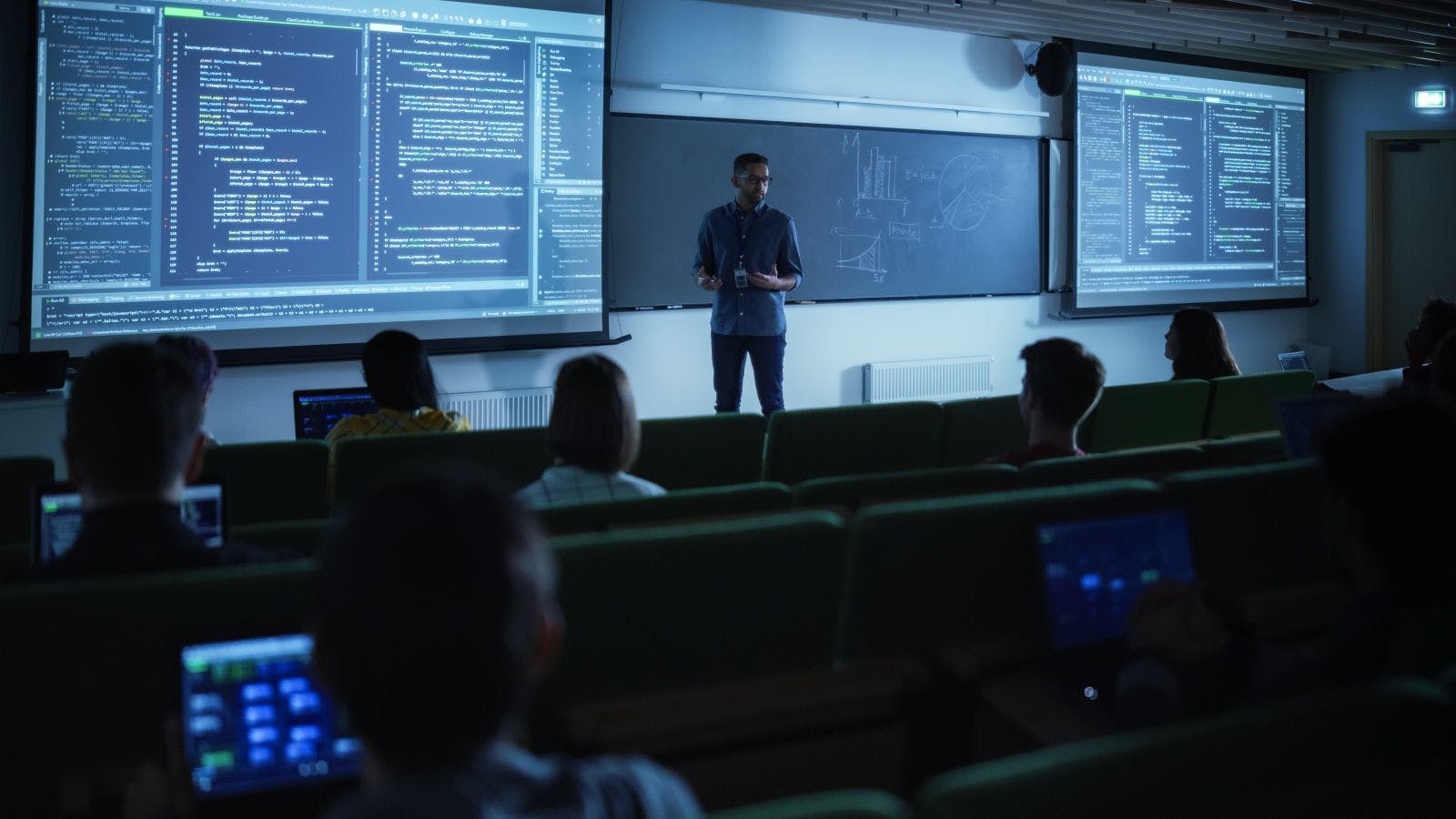 Young Male Teacher Giving a Data Science Lecture to Students in Dark College Room. Projecting Slideshow with Artificial Intelligence Architecture
