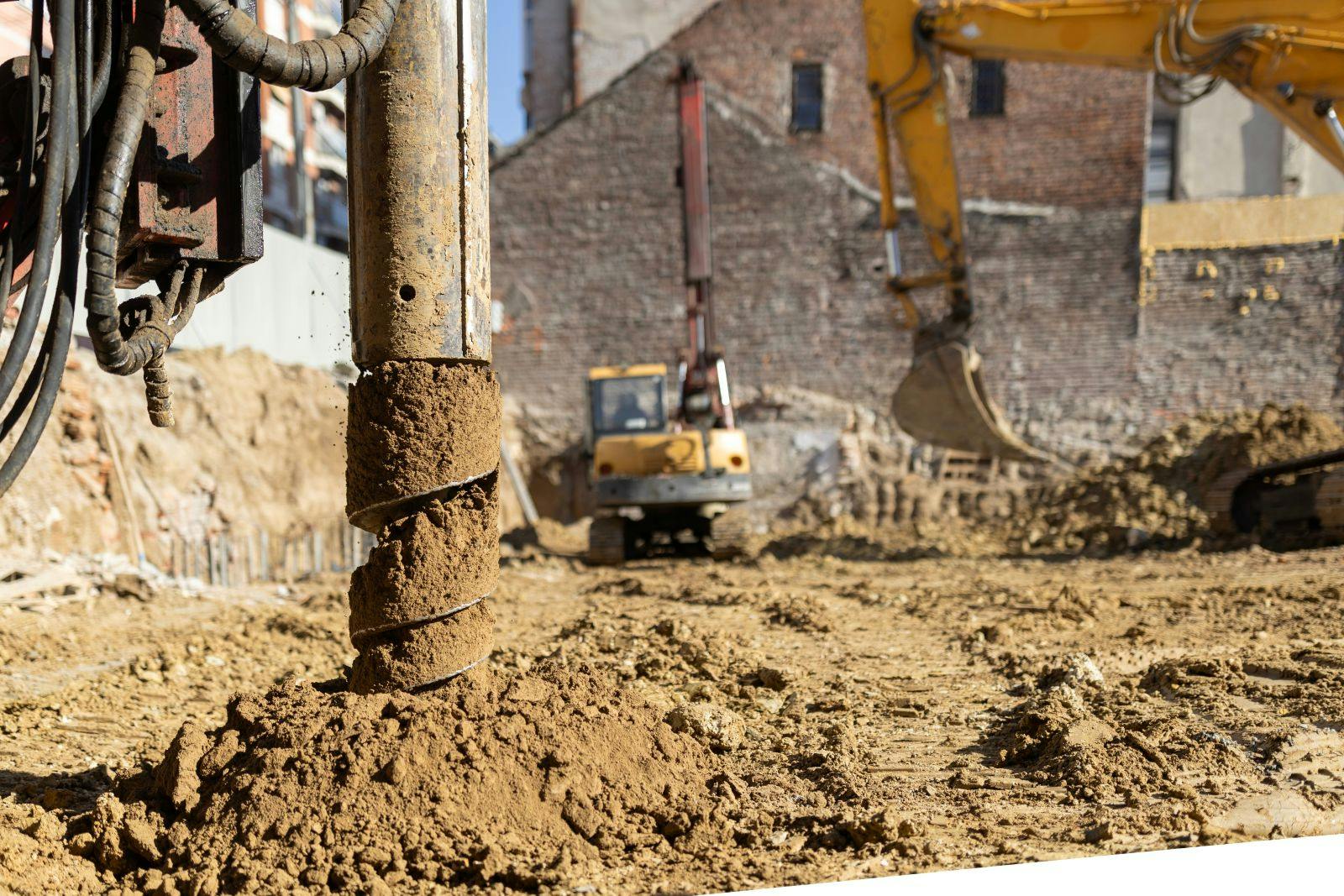 Industrial drilling rig auger creating a new building foundation at a development site with heavy machinery and excavated earth in an urban construction area