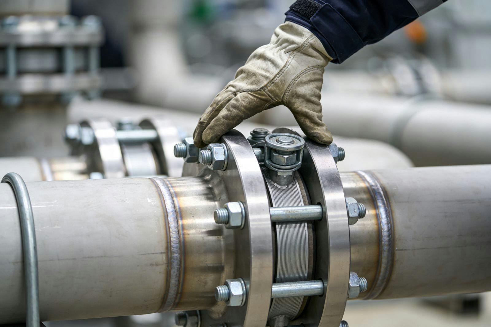 A worker wearing protective gloves carefully examines a secure flange joint on a large diameter industrial pipeline system