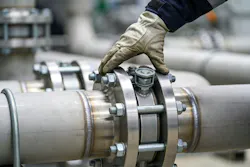 A worker wearing protective gloves carefully examines a secure flange joint on a large diameter industrial pipeline system