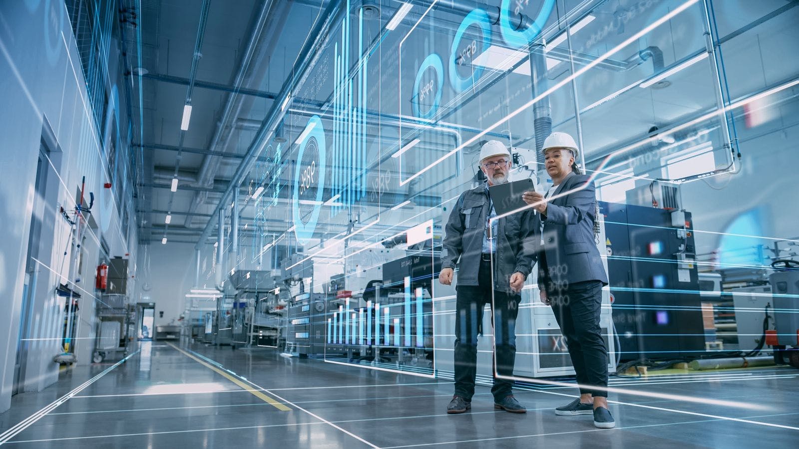 A digitalization concpt of two industrial engineers use a tablet computer to visualize a wall of big data statistics in a high-tech electronics facility.