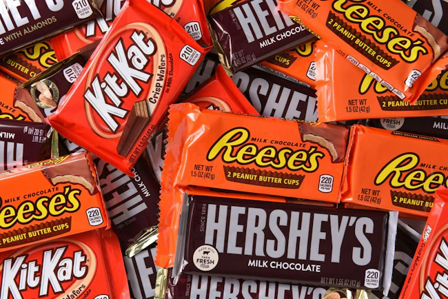 A close-up shot of a collection of Hershey's milk chocolate bars, Reese's cups and Kit Kat bars.