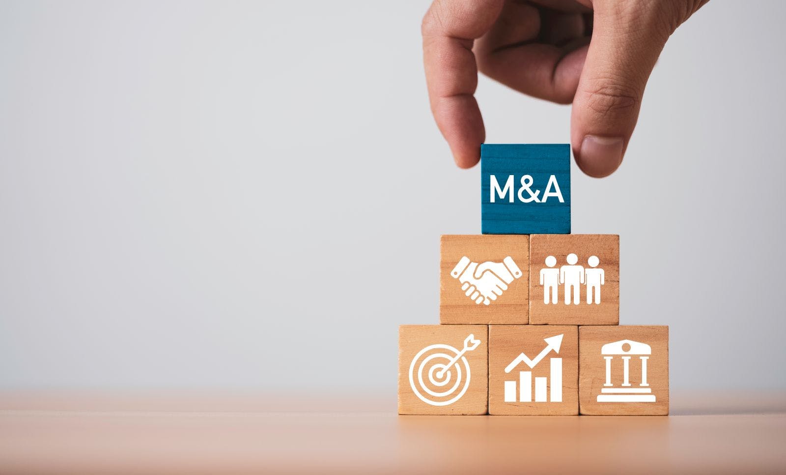 Hand placing M and A block on business strategy stack for mergers and acquisitions concept by representing corporate growth with partnership, investment strategy and financial performance.