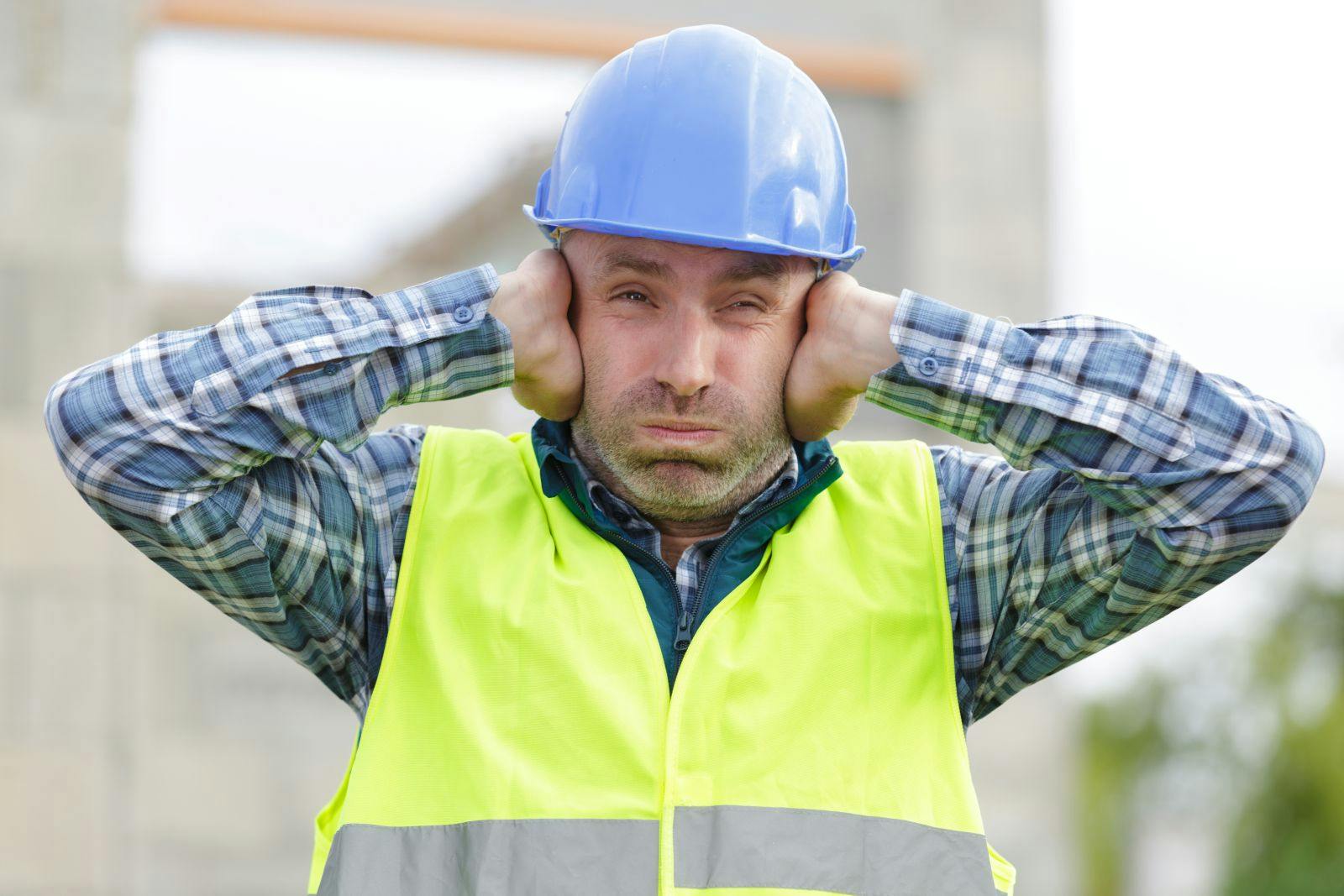 Construction worker holding his hands over his ears, suffering from noise pollution on building site