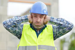 Construction worker holding his hands over his ears, suffering from noise pollution on building site