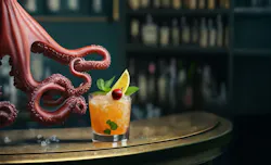 A maroon octopus is holding a tequila sunrise cocktail with its hand at the bar.