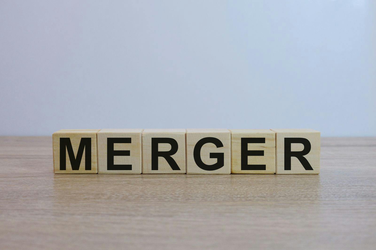 The word 'MERGER' spelled out on wooden blocks on a wooden surface