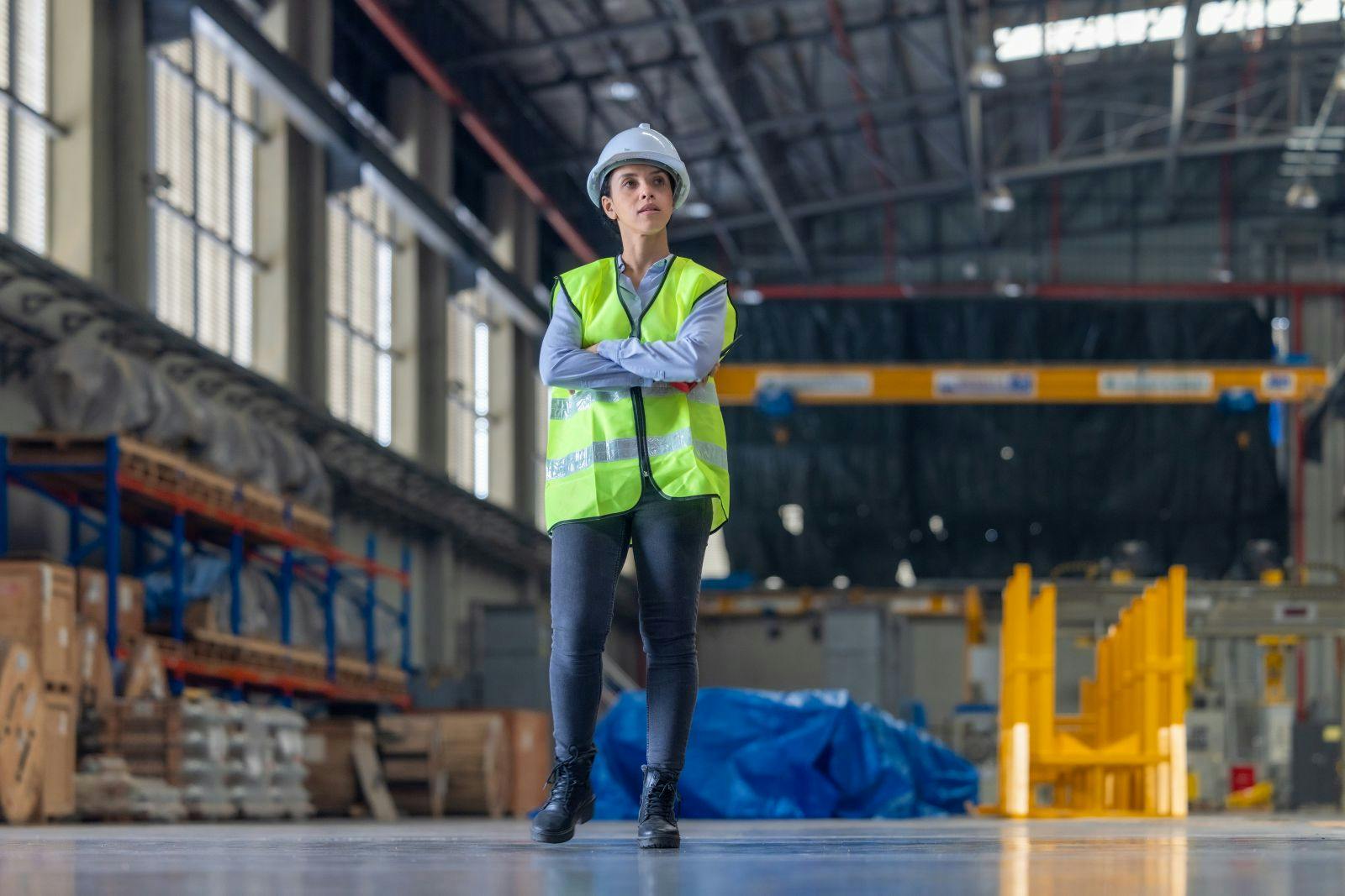Female engineer with hard hat and safety vest is seen from behind, observing train inside maintenance depot.