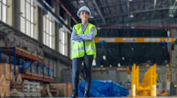 Female engineer with hard hat and safety vest is seen from behind, observing train inside maintenance depot.