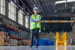 Female engineer with hard hat and safety vest is seen from behind, observing train inside maintenance depot.