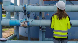 Female engineer inspecting water treatment pipelines with a digital tablet at a water supply plant. Concept of infrastructure, utility maintenance, water management and safety.