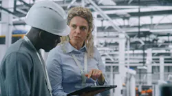 Two Specialists Solve Technical Issue in Vast Industrial Plant. Woman Points Area Concern on Factory Floor, Using Tablet For Data Reference. Problem Solving and Operational Excellence in Industry 4.0.