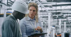 Two Specialists Solve Technical Issue in Vast Industrial Plant. Woman Points Area Concern on Factory Floor, Using Tablet For Data Reference. Problem Solving and Operational Excellence in Industry 4.0.