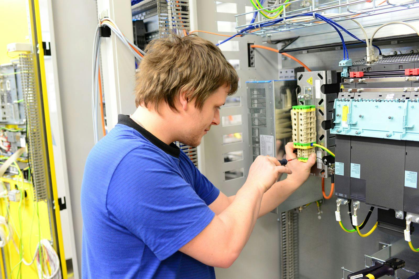 Young apprentice assembles components and cables in a factory in a switch cabinet - workplace industry with future