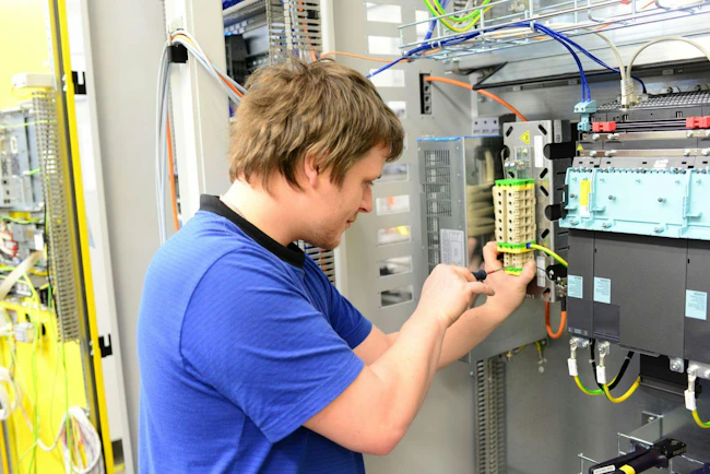 Young apprentice assembles components and cables in a factory in a switch cabinet - workplace industry with future