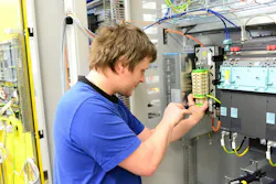 Young apprentice assembles components and cables in a factory in a switch cabinet - workplace industry with future
