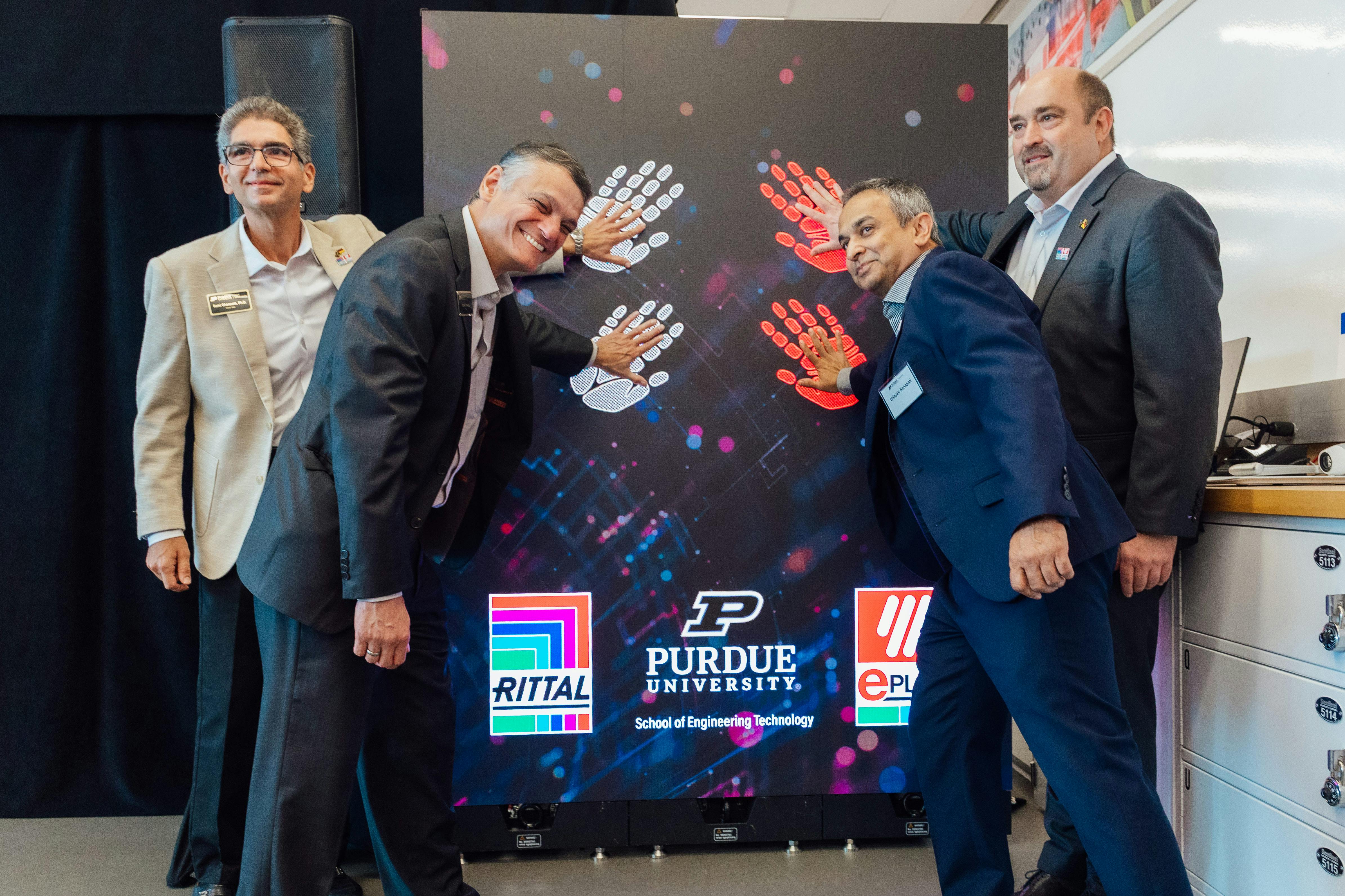 Four officials from Purdue, Rittal and Eplan placing their hands on a wall promoting their new engineering lab