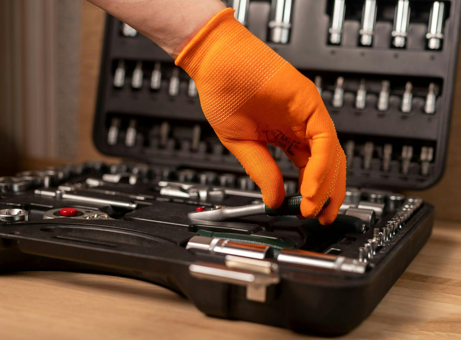 Male hand in building glove with socket ratchet handle, taken from toolbox. Industrial metal tool, close up on wooden background.
